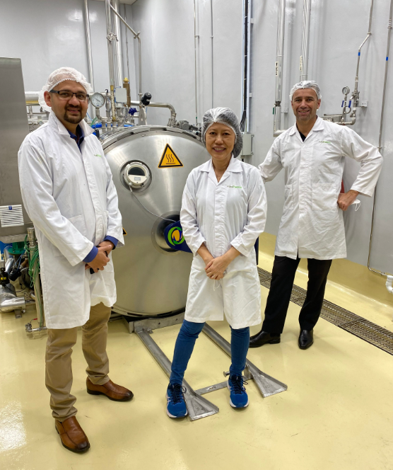 Photo of three people, 2 men and a woman in the centre, in white lab coats in a lab